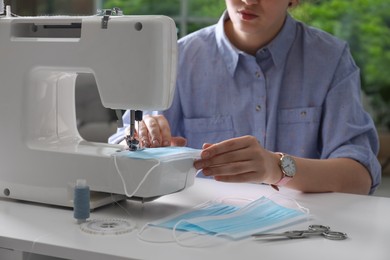 Photo of Woman sewing disposable protective mask with machine at table indoors, closeup