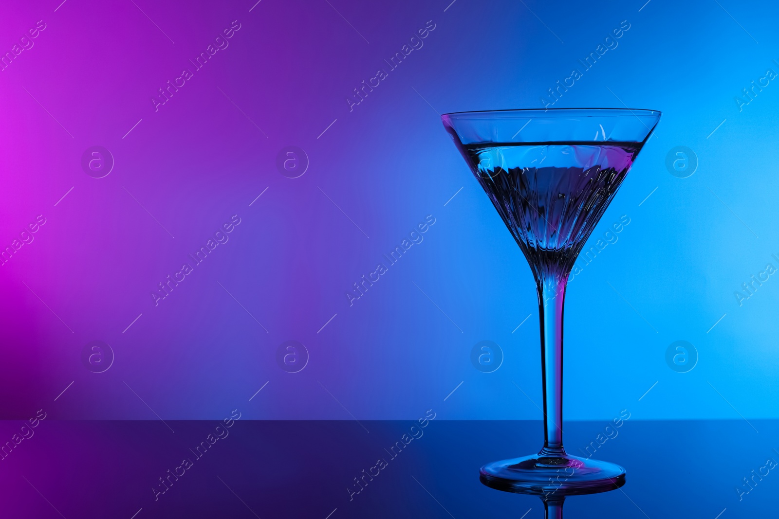 Photo of Fresh martini on table in neon lights, space for text