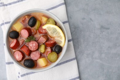 Meat solyanka soup with thin dry smoked sausages in bowl on grey table, top view. Space for text