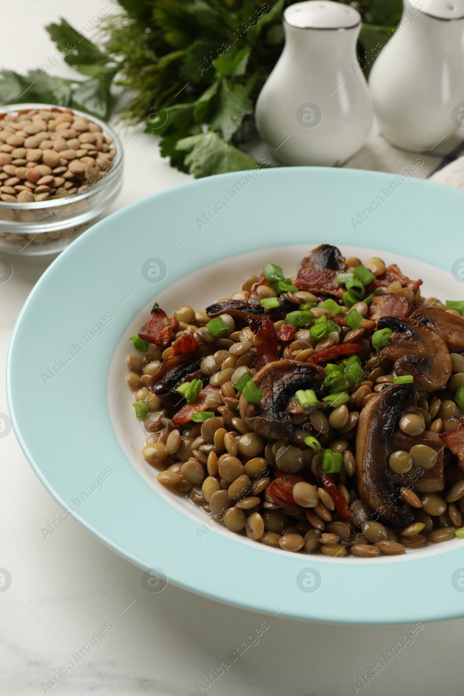 Photo of Delicious lentils with mushrooms, bacon and green onion on white table, closeup