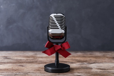 Photo of Retro microphone with red bow on wooden table against grey background. Christmas music