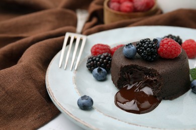 Photo of Delicious chocolate fondant served with fresh berries and fork on table, closeup