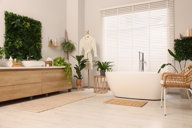 Photo of Green artificial plants, vanity and tub in bathroom