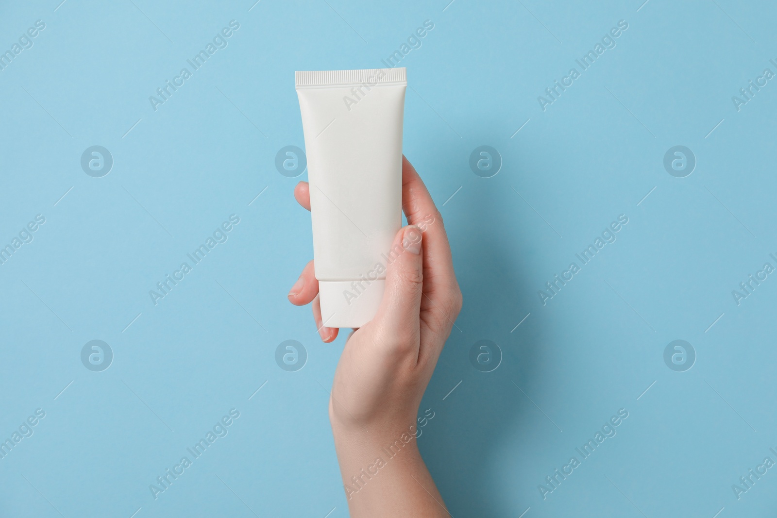 Photo of Woman with tube of hand cream on light blue background, top view