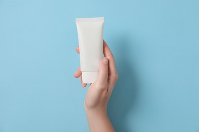 Woman with tube of hand cream on light blue background, top view