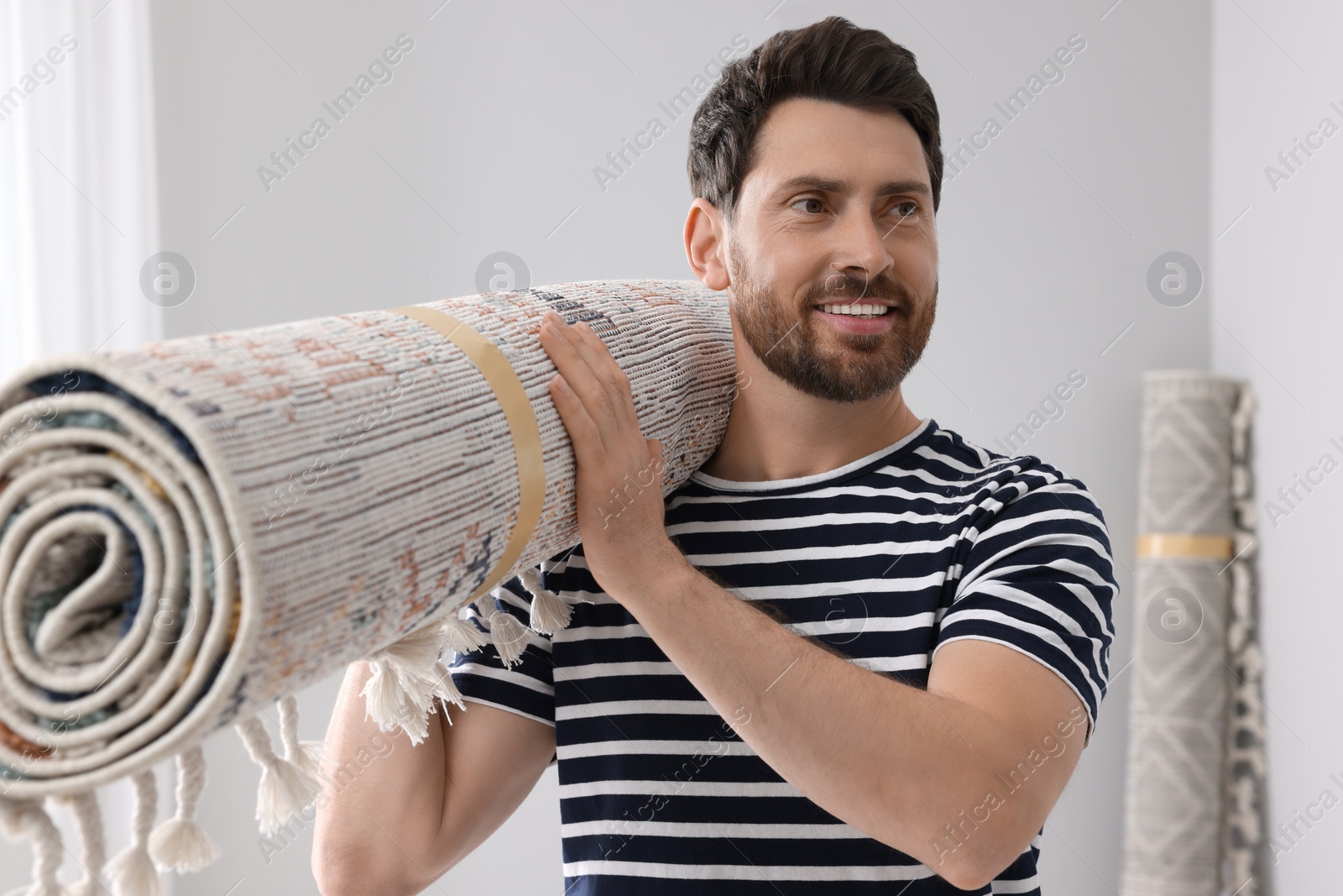 Photo of Smiling man holding rolled carpet in room