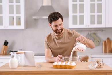 Photo of Man making dough while watching online cooking course via tablet in kitchen