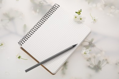 Photo of Guest list. Notebook, pencil and beautiful cherry tree blossoms on spring floral background, flat lay