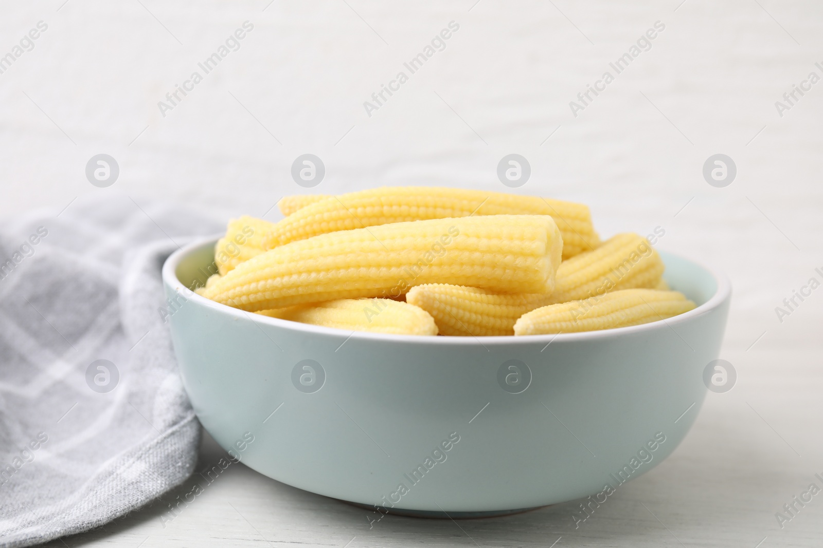 Photo of Tasty fresh yellow baby corns in bowl on white wooden table