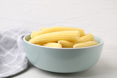 Photo of Tasty fresh yellow baby corns in bowl on white wooden table