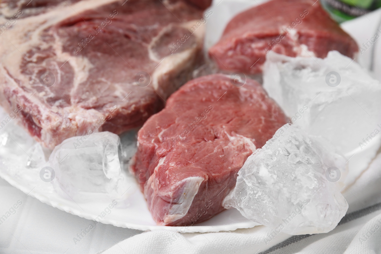 Photo of Fresh raw cut beef and ice cubes on white table, closeup