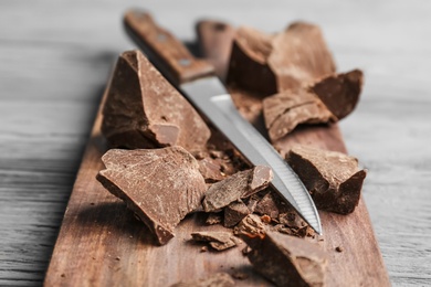 Pieces of delicious dark chocolate and knife on wooden board