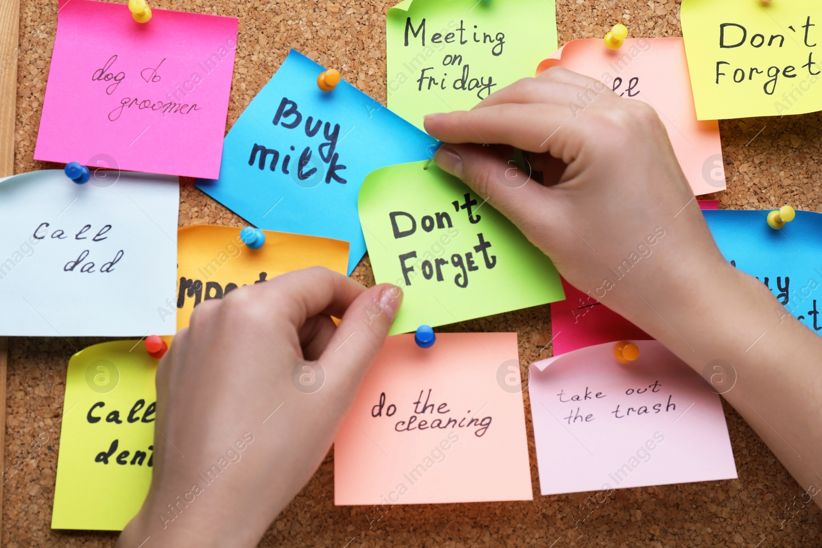 Photo of Woman pinning paper note with phrase Don't Forget to cork board, closeup