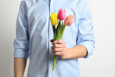 Man holding beautiful spring tulips on light background, closeup. International Women's Day