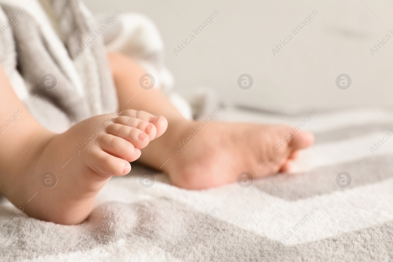 Photo of Little baby with cute feet on bed against light background, closeup. Space for text
