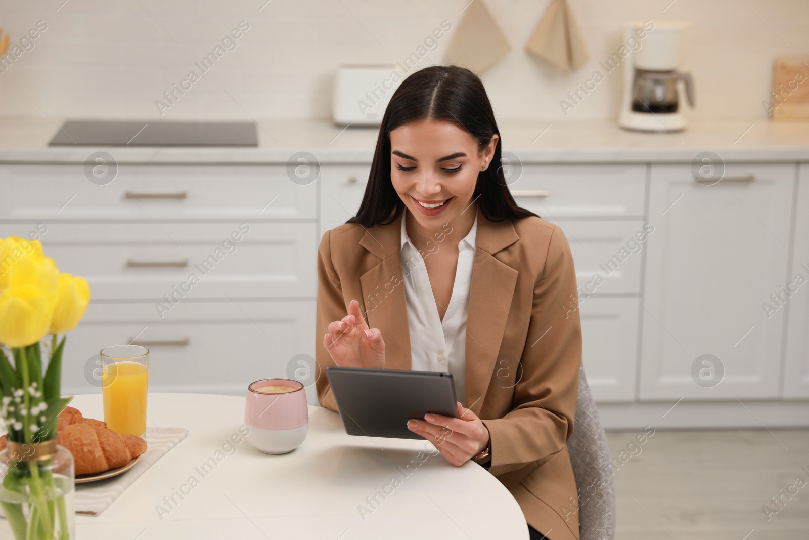 Photo of Young woman with tablet having breakfast in kitchen. Morning routine