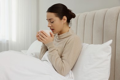 Photo of Sick young woman with cup of hot drink in bed at home