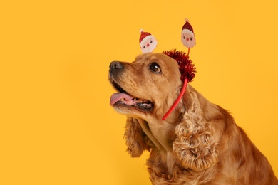 Photo of Adorable Cocker Spaniel dog in Santa headband on yellow background, space for text