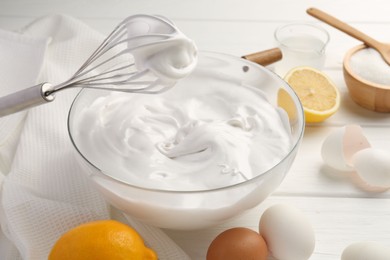Photo of Bowl with whipped cream, whisk and ingredients on white wooden table