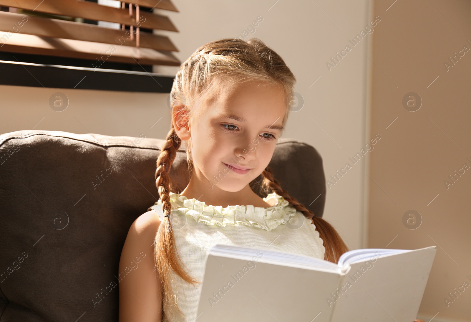 Photo of Little girl reading book in armchair at home