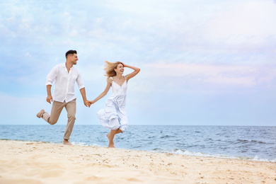 Happy couple running on beach, space for text. Romantic walk