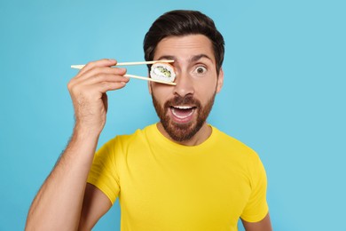 Funny man hiding his eye with tasty sushi roll on light blue background