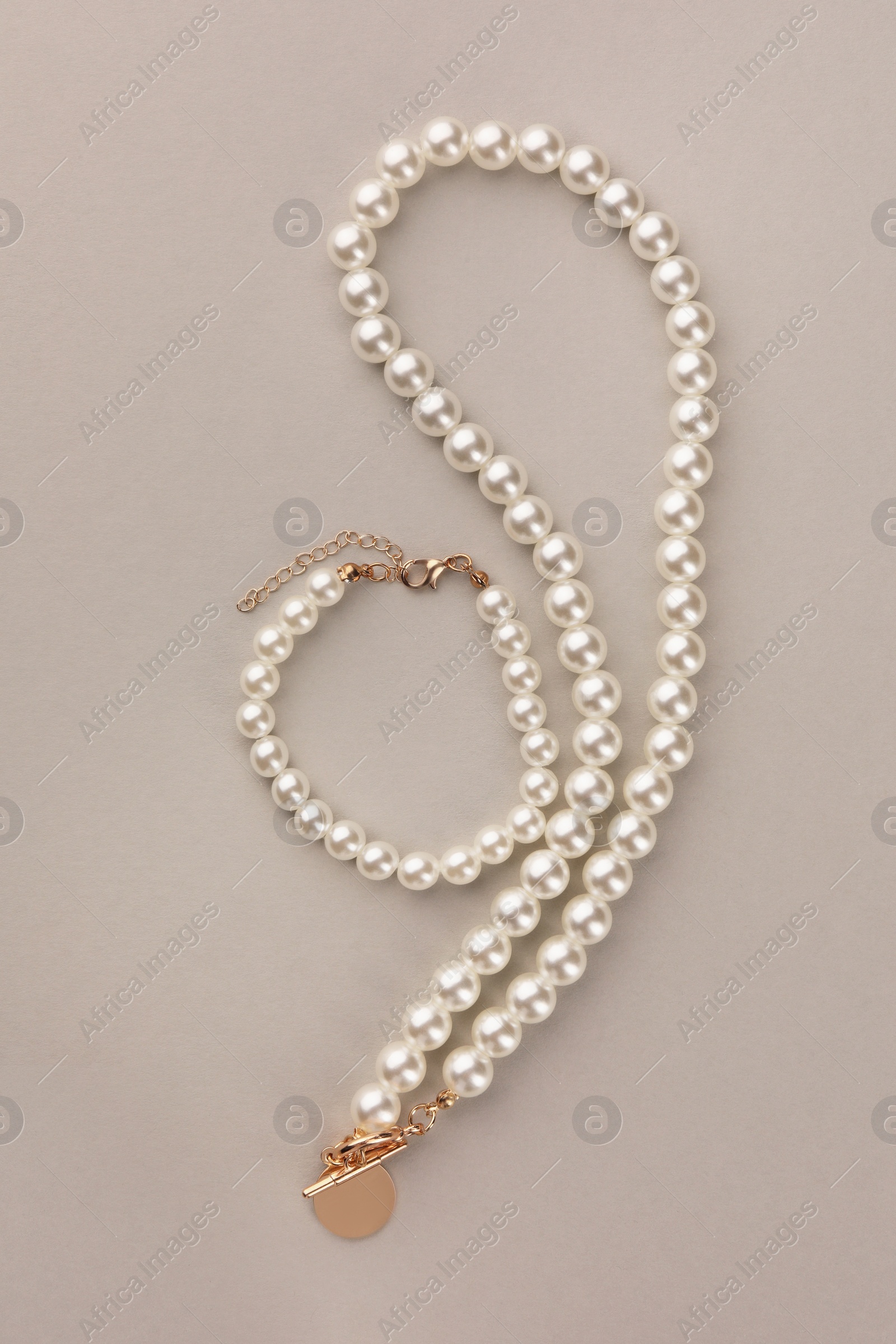 Photo of Elegant pearl necklace and bracelet on beige background, top view