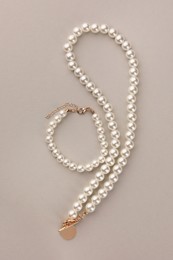 Photo of Elegant pearl necklace and bracelet on beige background, top view