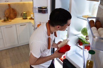 Man with sauces and sausages near refrigerator in kitchen