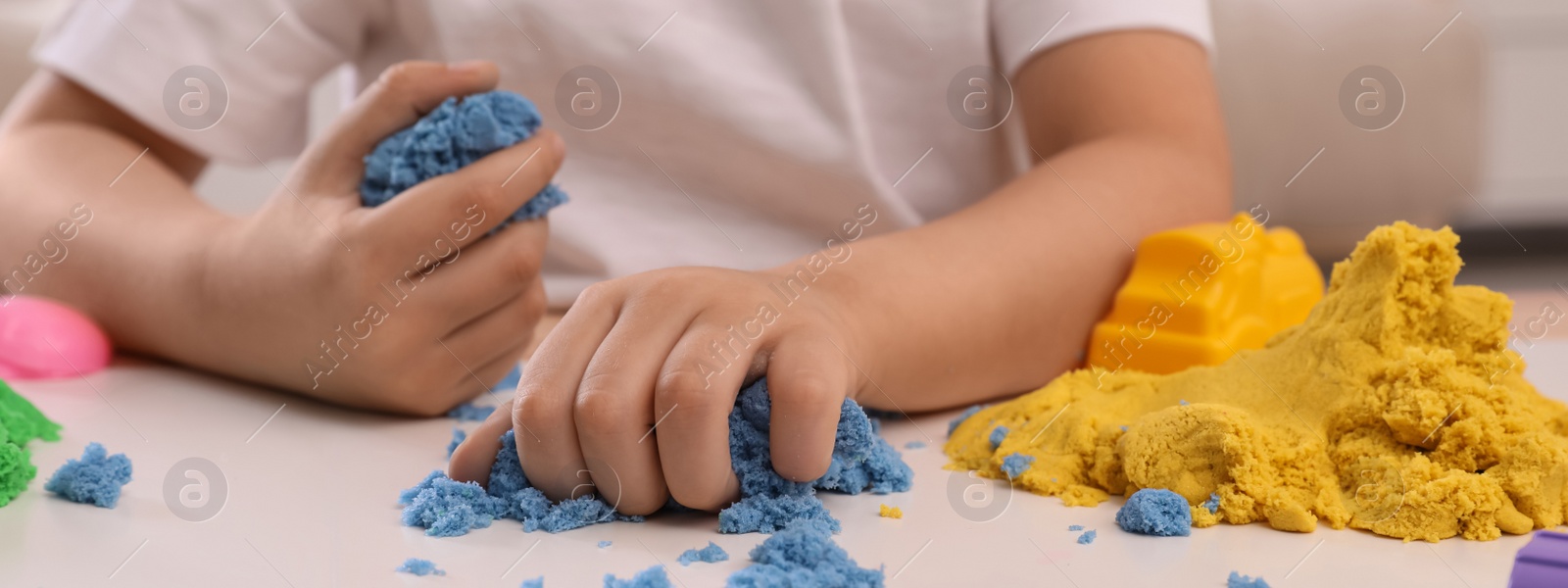 Image of Little boy playing with bright kinetic sand at table indoors, closeup. Banner design