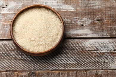 Photo of Raw basmati rice in bowl on wooden table, top view. Space for text