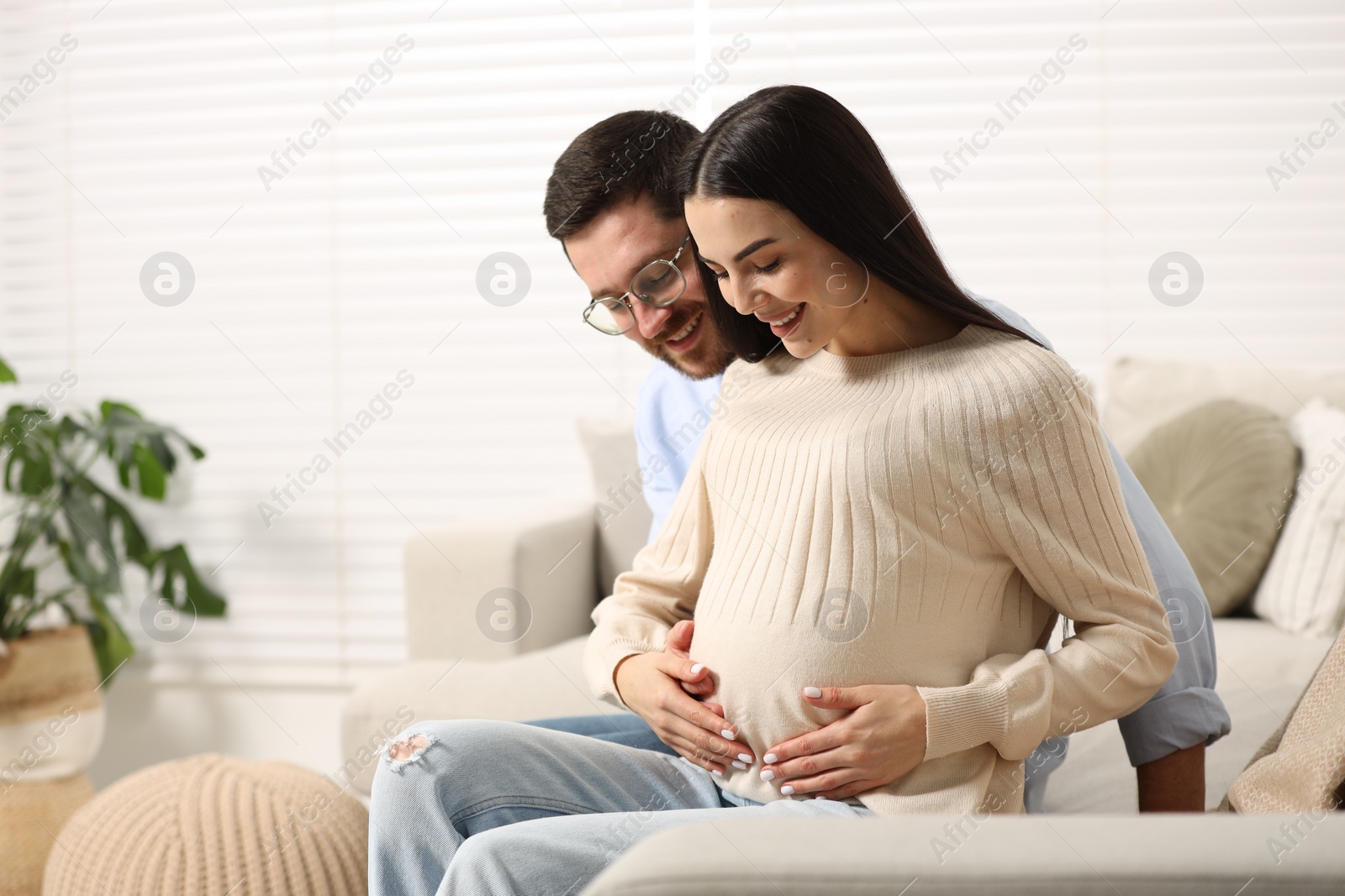 Photo of Happy pregnant woman spending time with her husband on sofa at home