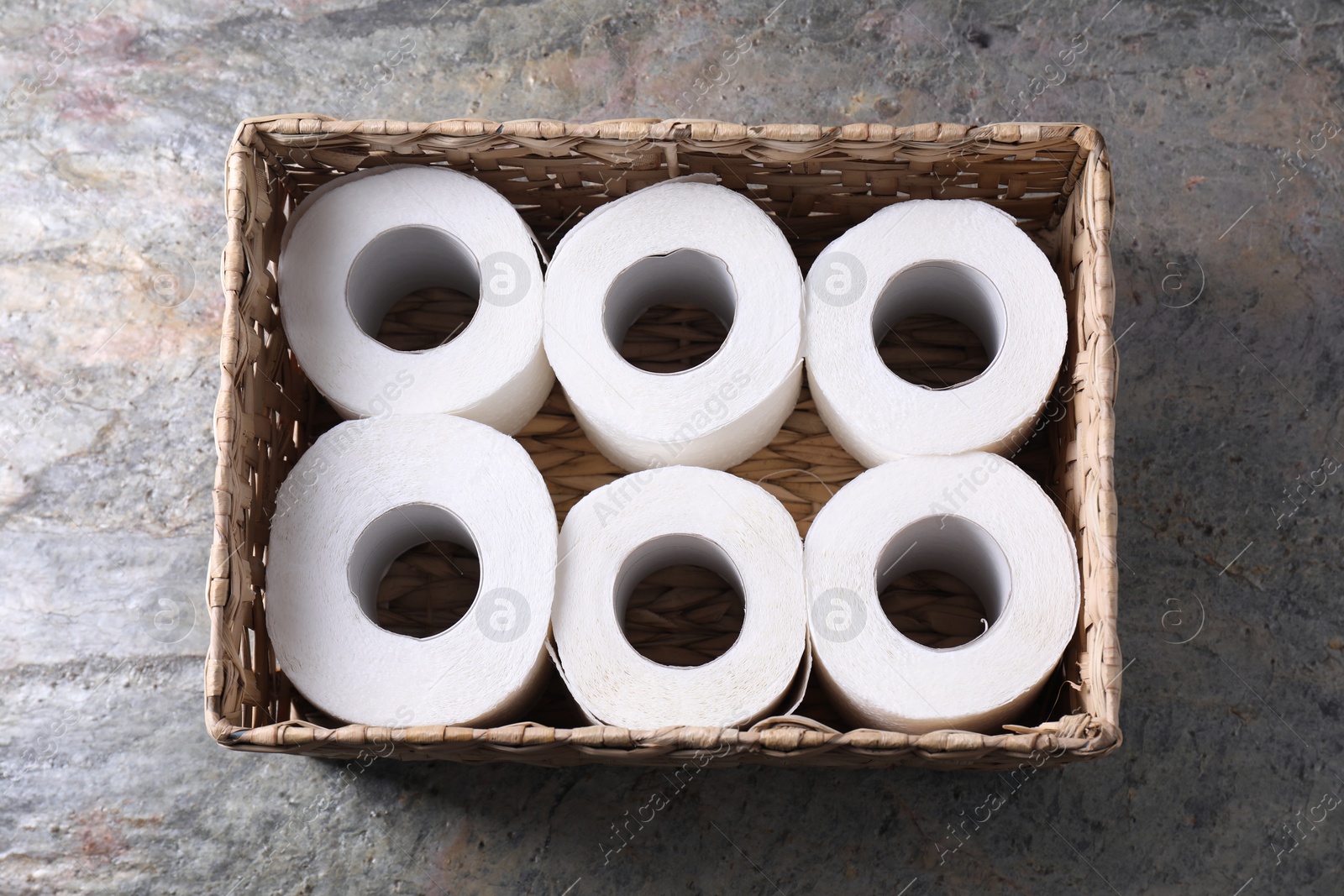 Photo of Toilet paper rolls in wicker basket on textured table, top view