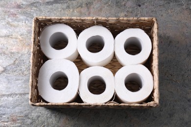 Photo of Toilet paper rolls in wicker basket on textured table, top view