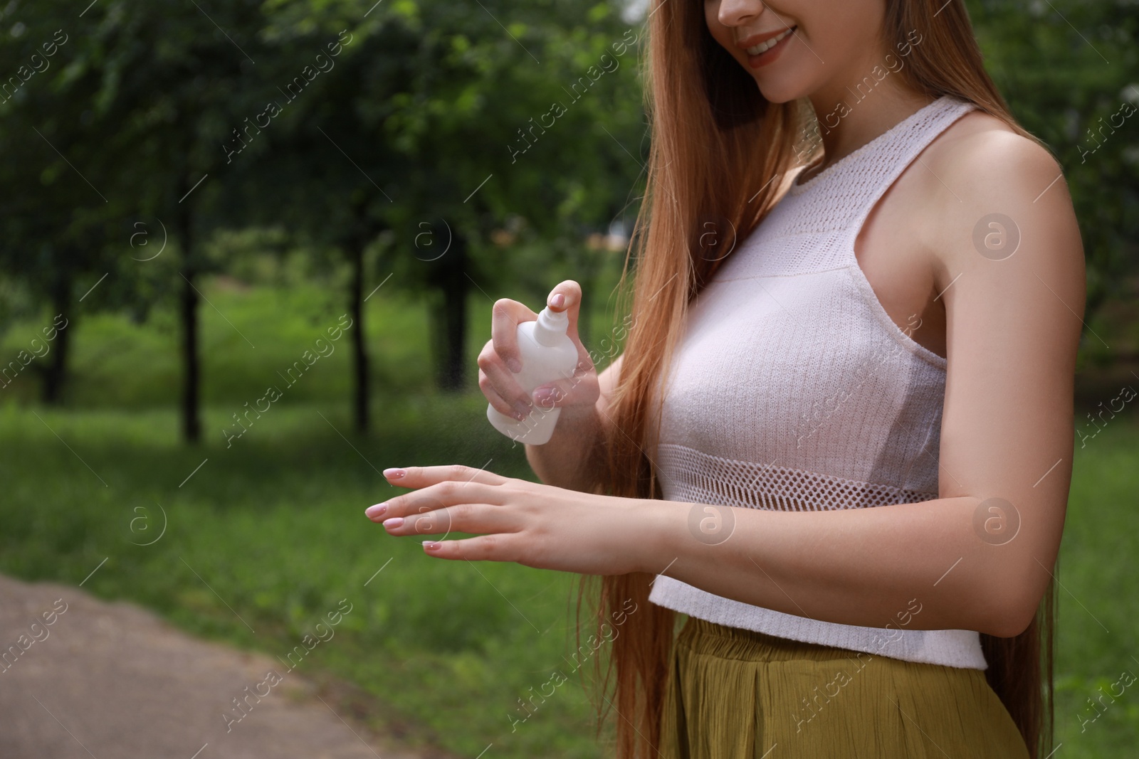 Photo of Woman applying insect repellent onto hand in park, closeup. Tick bites prevention