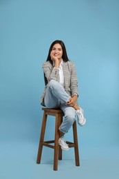 Photo of Beautiful young woman sitting on stool against turquoise background