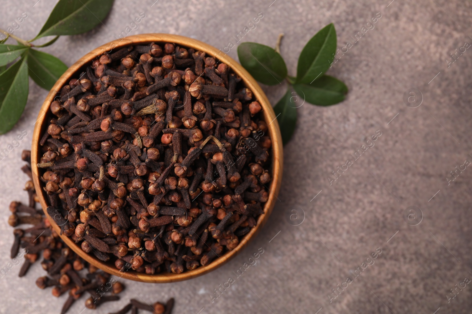 Photo of Aromatic cloves and green leaves in bowl on brown table, top view. Space for text