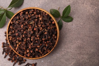 Aromatic cloves and green leaves in bowl on brown table, top view. Space for text