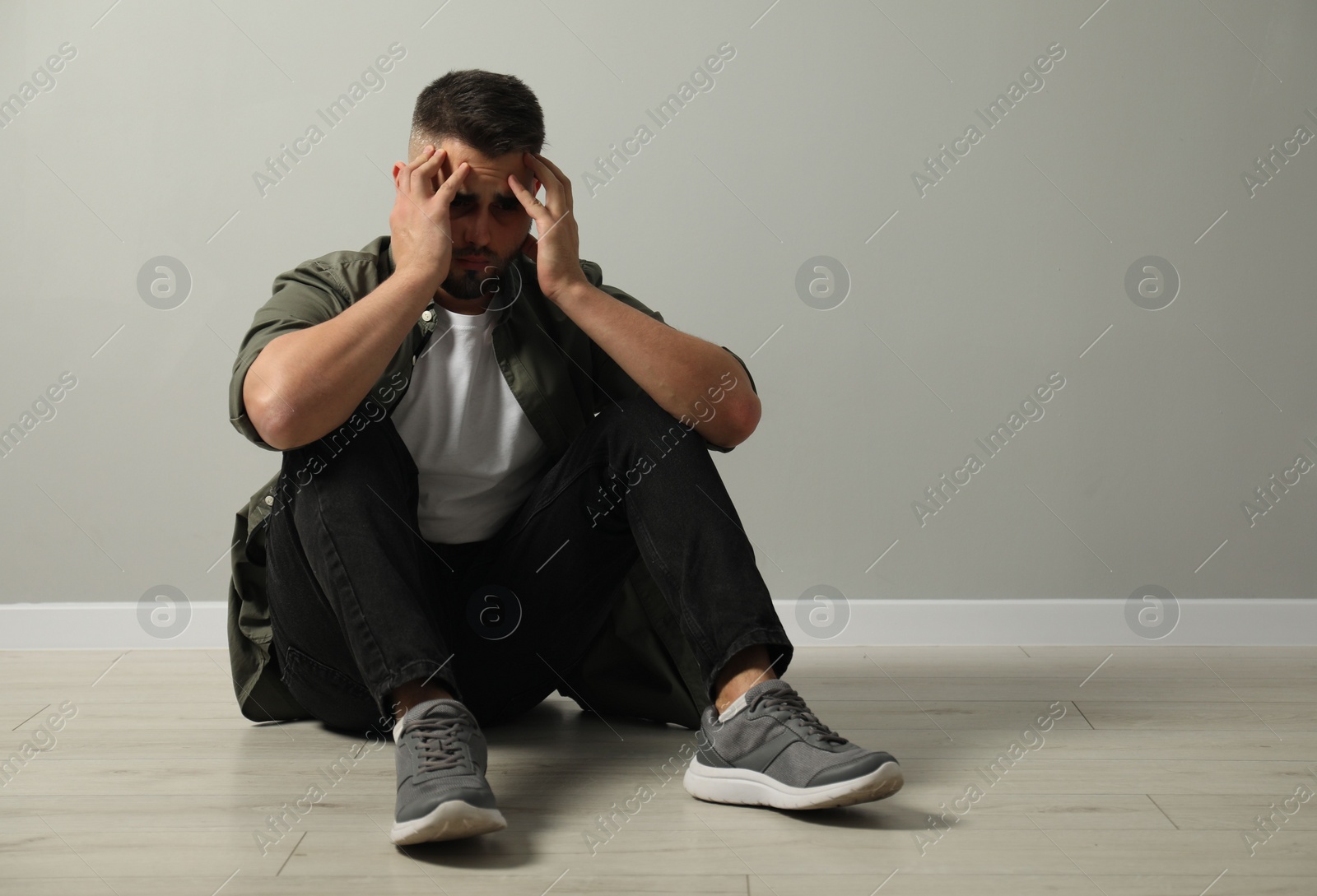 Photo of Sad man sitting on floor near light grey wall. Space for text