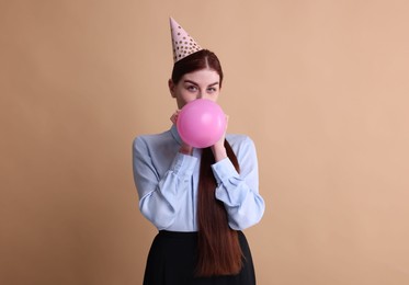 Photo of Young woman in party hat blowing balloon on beige background