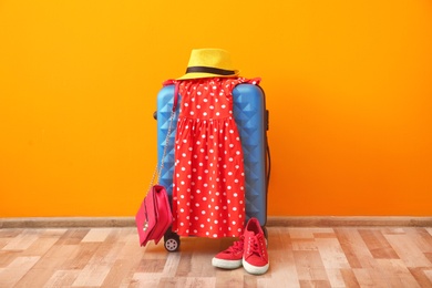 Packed suitcase, dress and shoes prepared for summer journey on floor near color wall