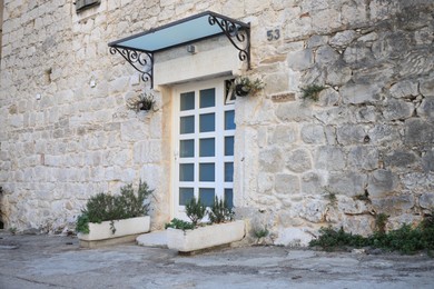 Photo of Entrance of residential house with white door in stone wall and potted plants
