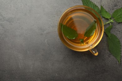 Photo of Glass cup of aromatic nettle tea and green leaves on grey table, flat lay. Space for text