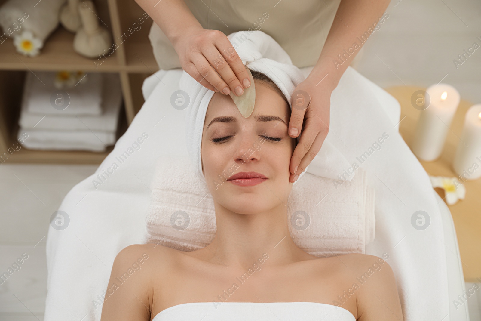 Photo of Young woman receiving facial massage with gua sha tool in beauty salon