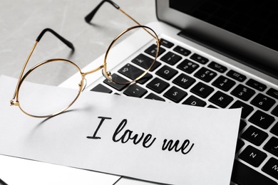 Paper with handwritten phrase I Love Me and glasses on laptop, closeup