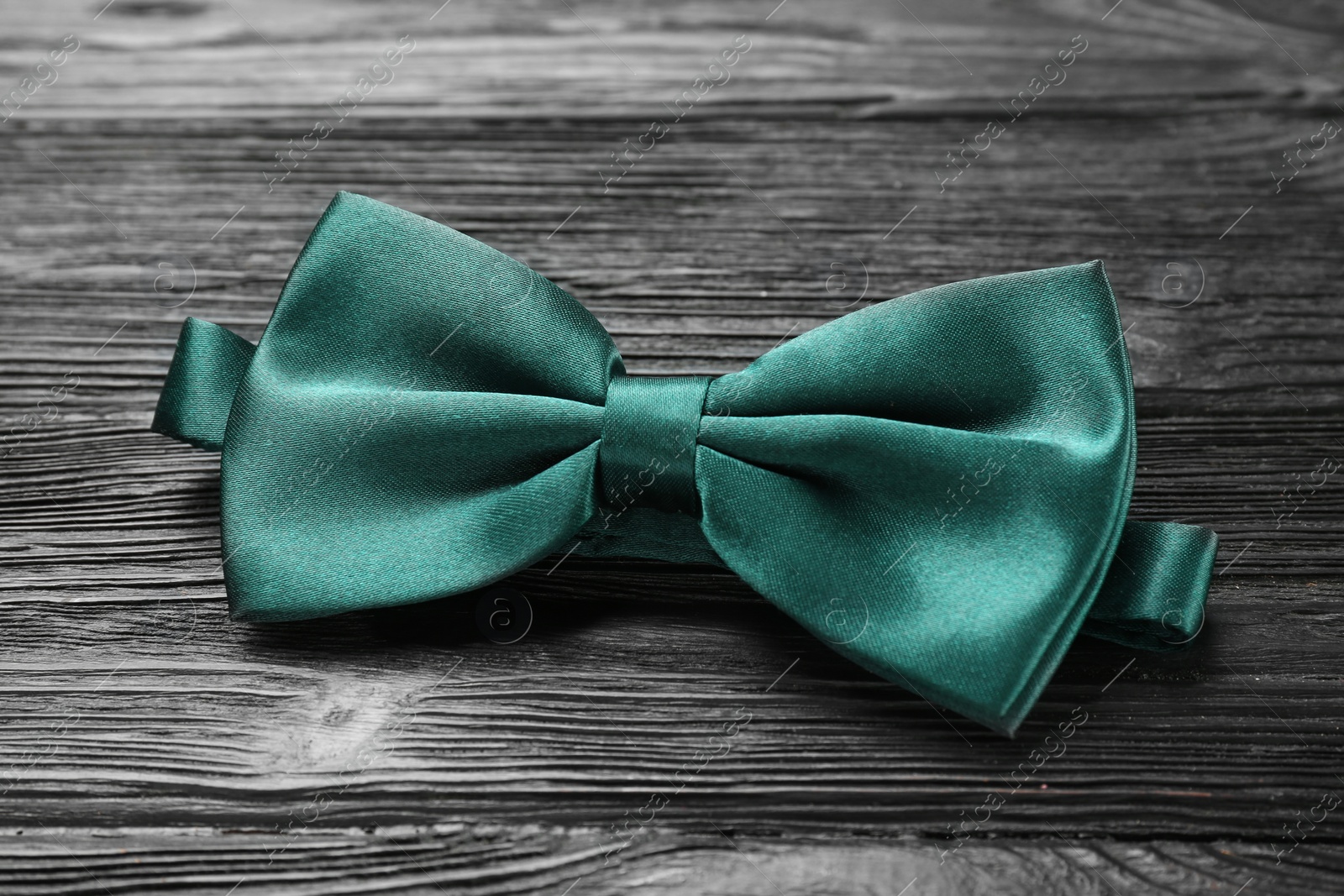 Photo of Stylish green satin bow tie on black wooden background, closeup