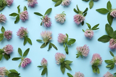 Photo of Beautiful clover flowers with green leaves on light blue background, flat lay