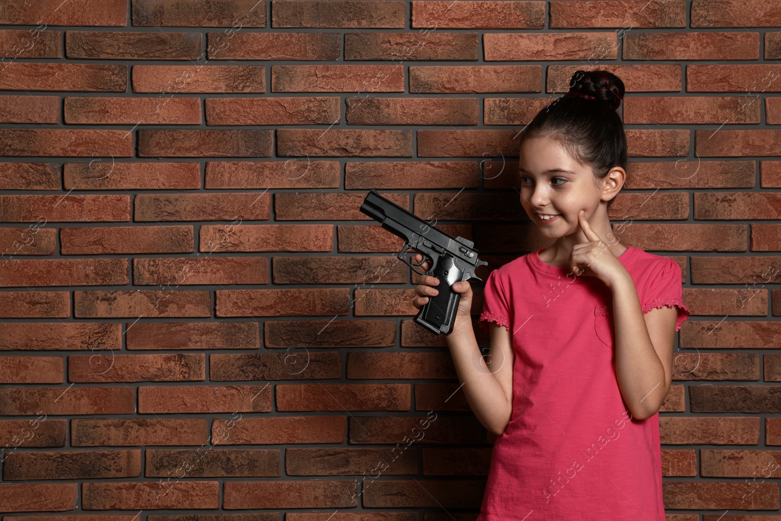 Photo of Little child playing with gun against brick wall, space for text. Dangerous game