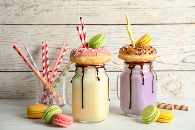 Photo of Mason jars with delicious milk shakes and macaroons on table