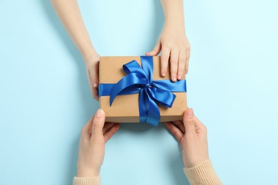 Photo of Mother giving gift box to her child on light blue background, top view